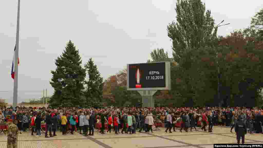 На площади Ленина стоят в ряд 17 закрытых гробов с телами жертв трагедии.Рядом с каждым из них - фотографии и таблички с именами погибших. Играет траурная музыка. На большом экране изображена свеча и надпись &laquo;Керчь 17.10.2018&raquo;